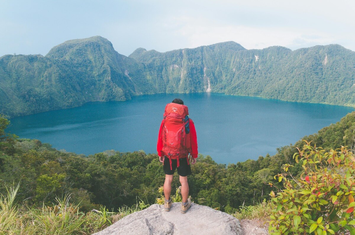 Man carrying red backpack standing on a mountain facing  the lake