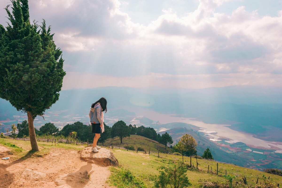 Woman in blue jacket standing face down on a hill with a tree on her back
